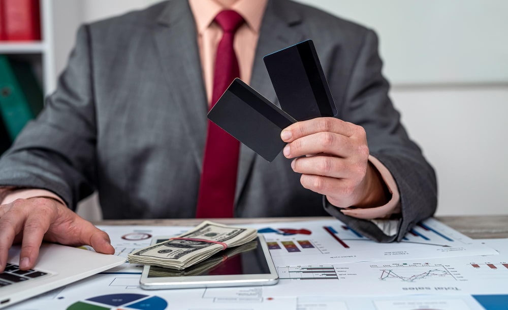 Homme d'affaires tenant des cartes bancaires au-dessus de billets et de graphiques, illustrant la gestion de la liquidité bancaire