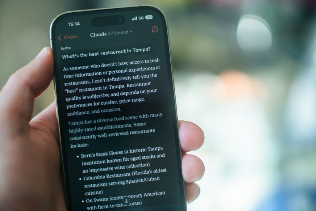 Main tenant un smartphone affichant une conversation avec Claude 3.7 Sonnet sur les recommandations de restaurants, illustrant les dernières news intelligence artificielle en matière de modèles conversationnels.