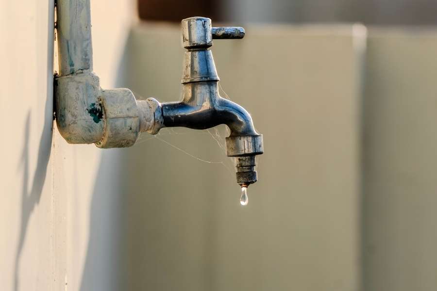 Un vieux robinet mural rouillé fuit et goutte, ce qui suggère que l'eau de robinet sent mauvais.