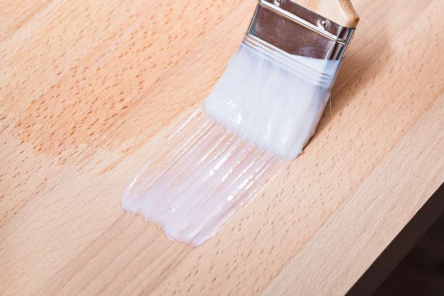 Un pinceau applique une couche de protection transparente en choisissant le bon vernis pour plan de travail en cuisine.