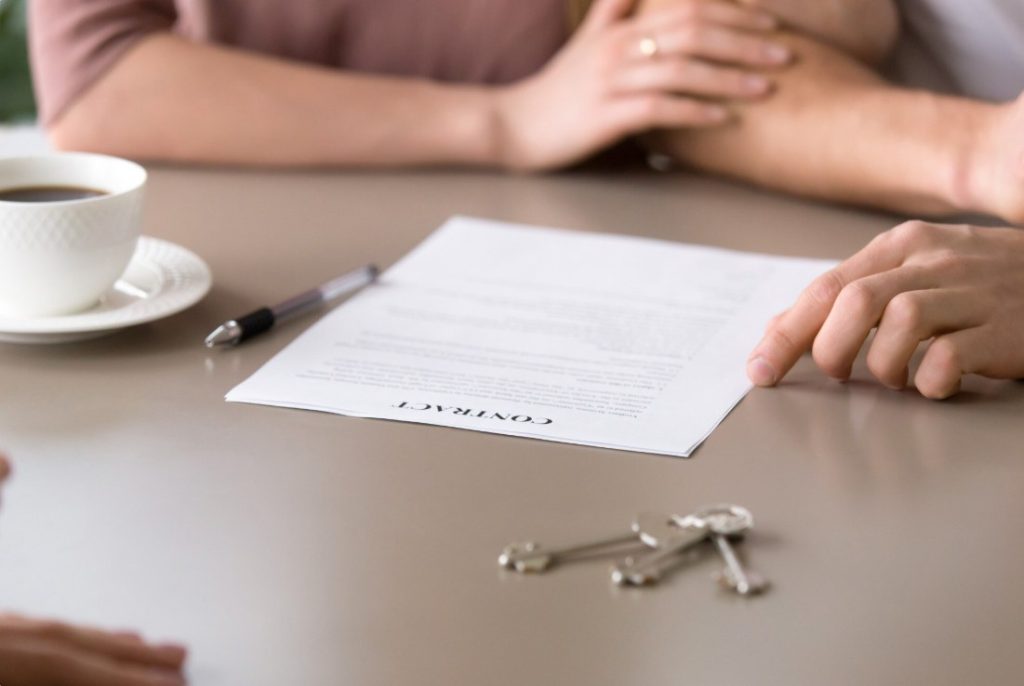 Un couple assis autour d'une table avec un contrat, des clés et une tasse de café lors de l'acquisition immobilière et du calcul des frais de notaire dans l'ancien.